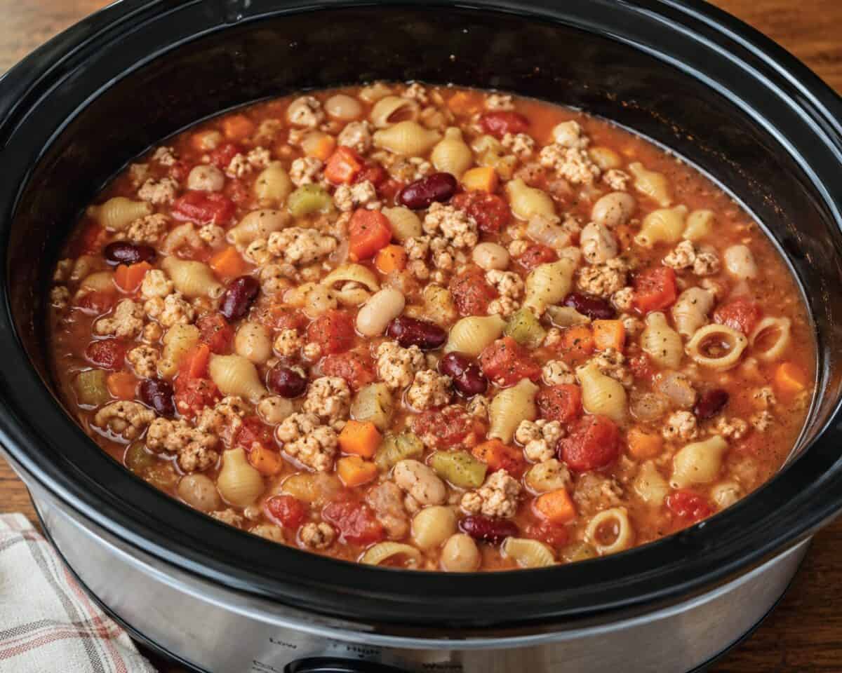 Cooking slow cooker chicken pasta fagioli in black crock pot.
