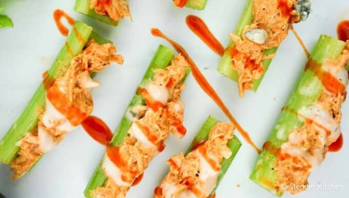 buffalo chicken filled celery sticks arranged on a diagonal on white plate with drizzle of buffalo sauce