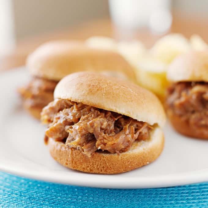 Barbecue chicken sliders on white plate up close.