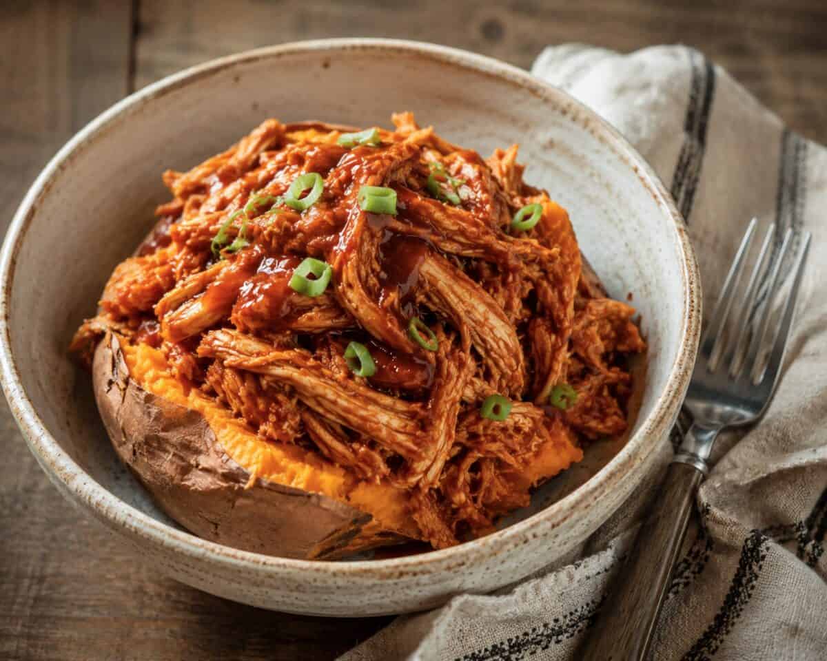 Slow cooker bbq chicken topped baked sweet potato garnished with sliced green onion.