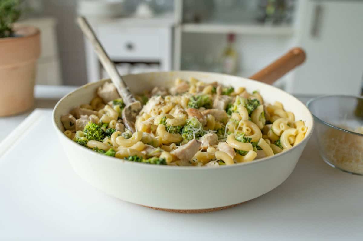 Macaroni pasta with broccoli and chicken and grated Parmesan cheese in saucepan with wooden spoon.