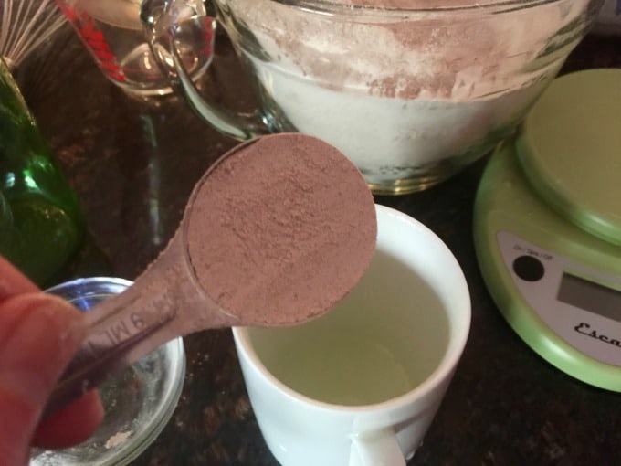 Measuring tablespoon of cake mix into a white mug with bowl of cake mix in background