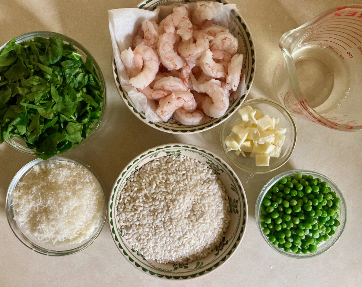 Easy Oven Risotto Ingredients on Counter: Shrimp, Arborio Rice, Chopped Spinach, Grated Parmesan Cheese, Cubes of Butter, Peas, Chicken Broth
