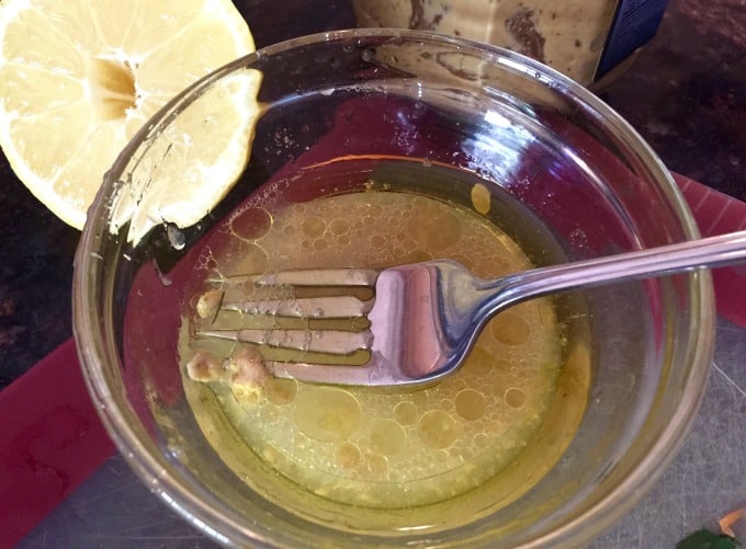 Clear bowl with lemon juice, mustard, olive oil and fork for whisking