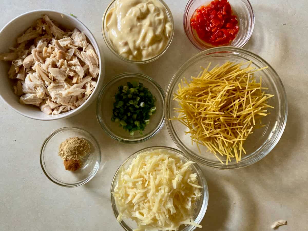 Bowls of broken spaghetti, shredded cooked chicken, chopped pimentos, cream of chicken soup, shredded cheese, spices, chopped green onion