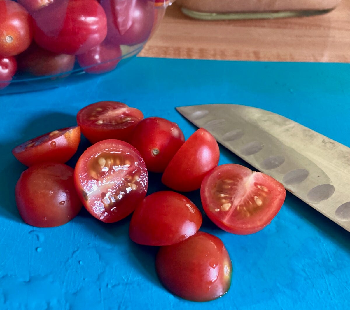 Halved cherry tomatoes on blue cutting boaard