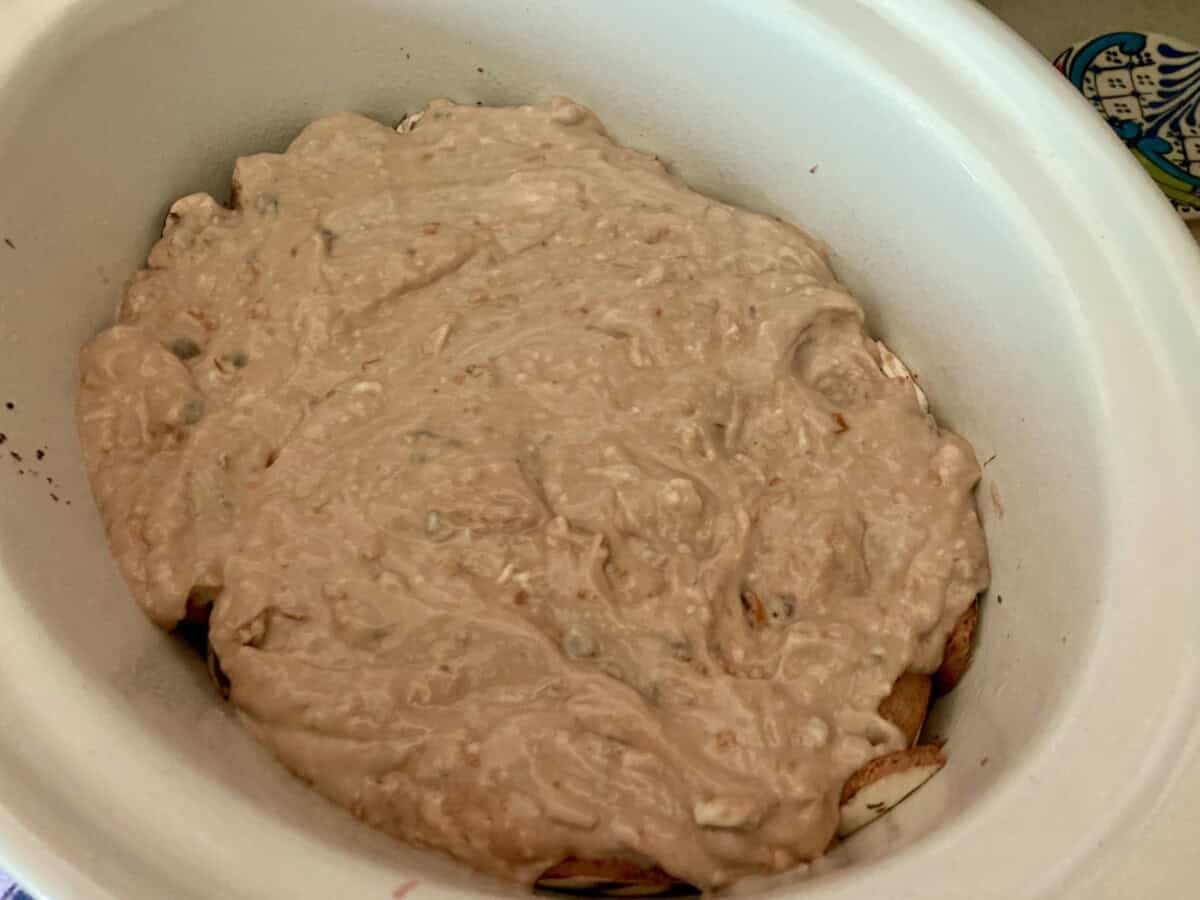Beef topped with mushroom soup, onion soup, red wine mixture in crockpot ready to cook.