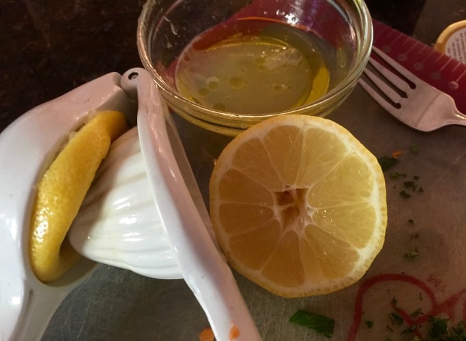 Squeezing fresh lemon juice from halved lemon into glass bowl.