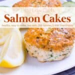 Two salmon cakes with lemon wedges on white dinner plate.