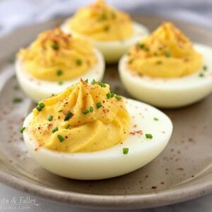 a pottery plate with deviled eggs garnished with paprika and chives shot from front
