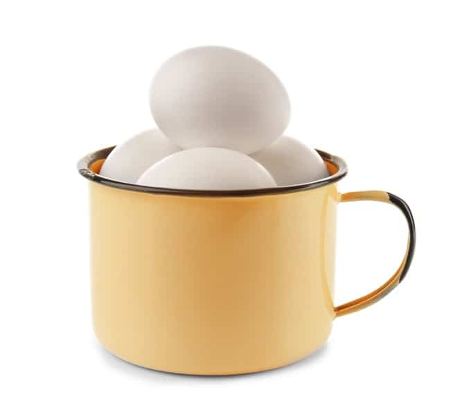 Raw whole eggs in yellow mug on white background