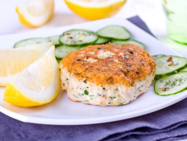 Close up of a salmon cake served with cucumber and lemon