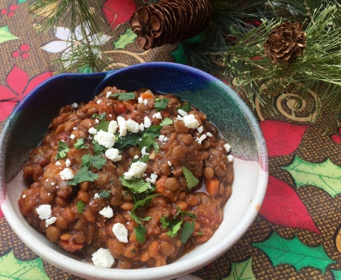 Bowl of Vegetarian Lentil Chili garnished with feta cheese and cilantro on a Christmas tablecloth