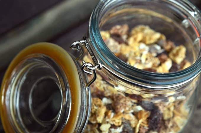 Muesli with dried fruit in glass jar with lid open.