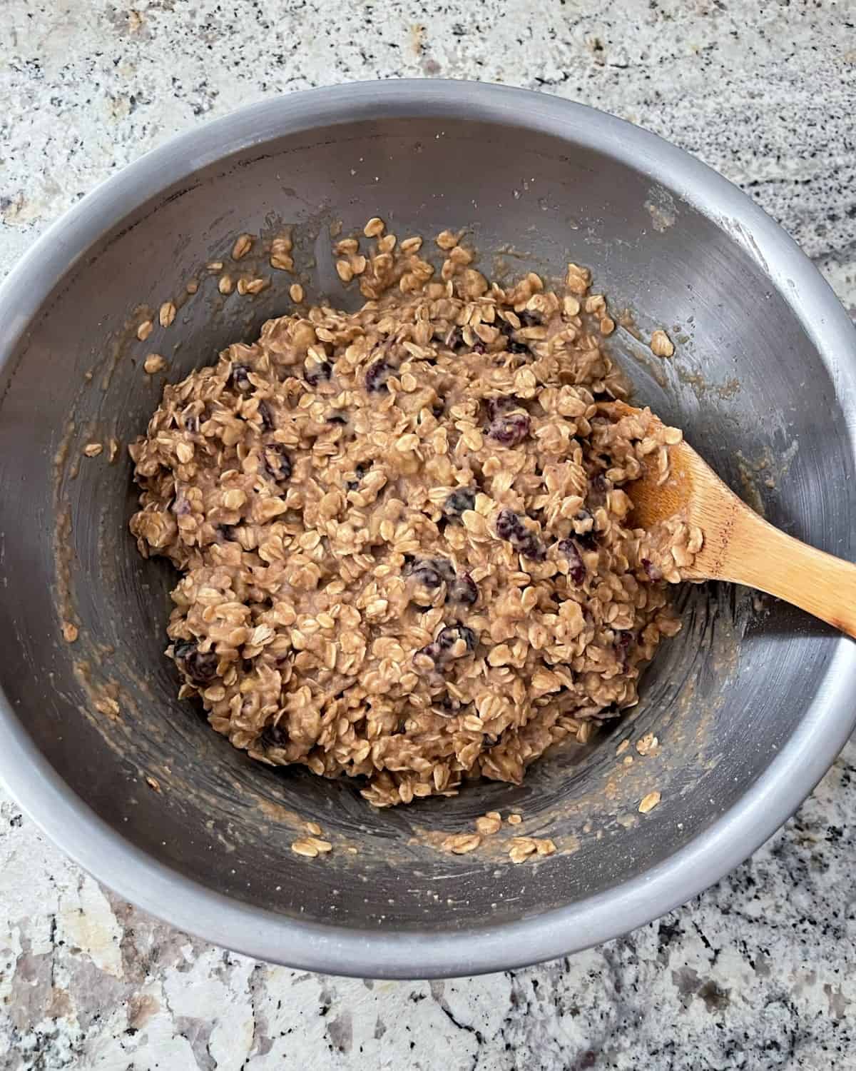 Mixing applesauce oatmeal cookie dough in a mixing bowl with wooden spoon.