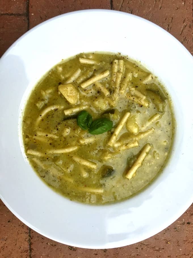 Bowl of Italian soup with zucchini and pesto on a red brick background
