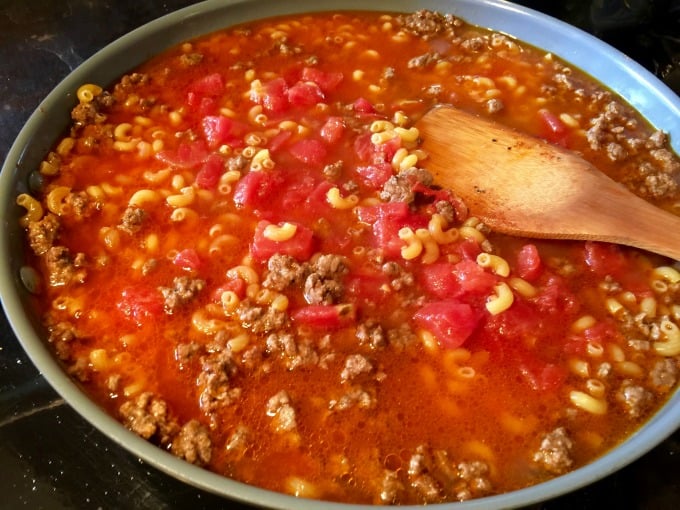 Ground beef, tomatoes, broth, macaroni in skillet wooden spoon.