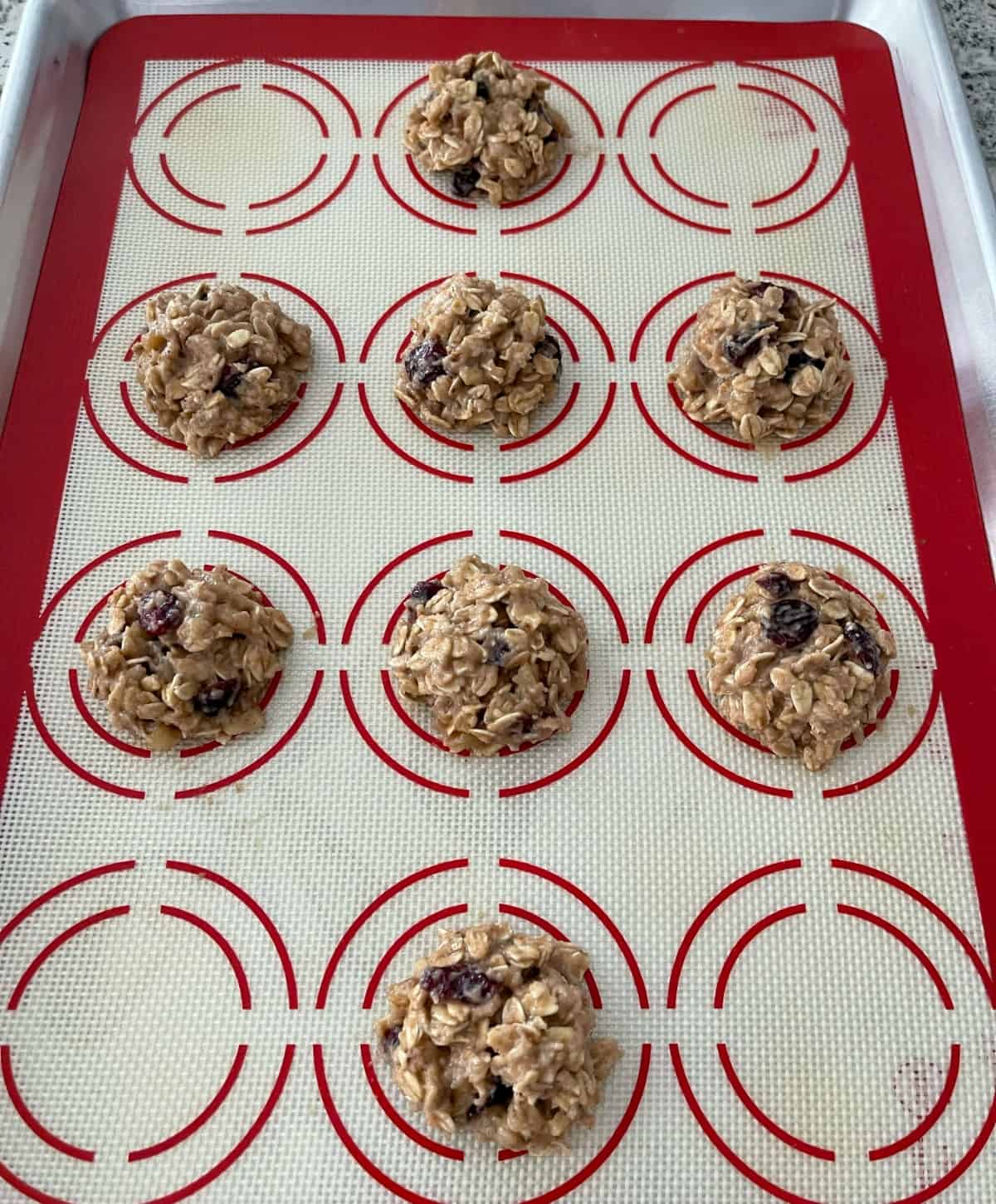 Unbaked applesauce oatmeal cookies on silpat lined baking sheet.