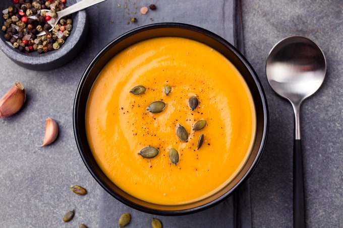 Curried carrot apple soup with pumpkin seeds on grey stone background