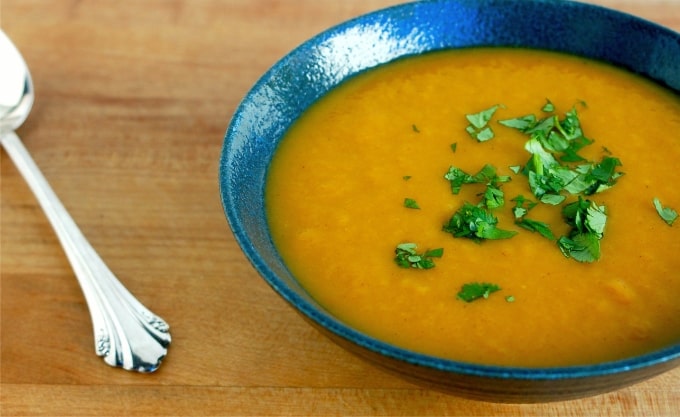 Curried carrot soup topped with fresh herbs in blue ceramic bowl.