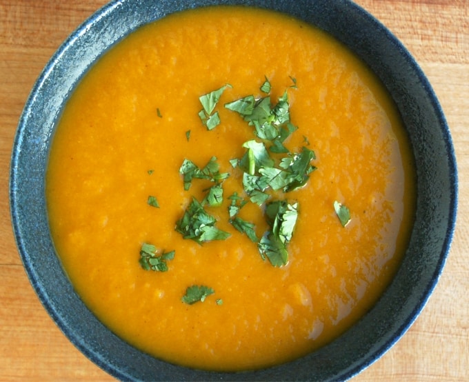 Crock pot curried carrot apple soup with fresh cilantro in blue ceramic bowl from above.