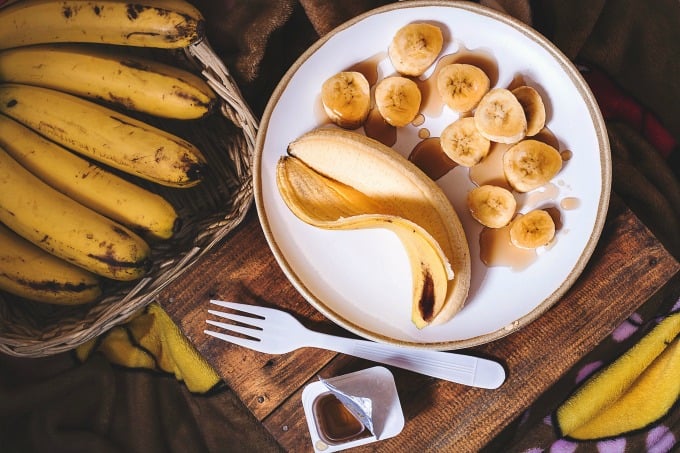 A bunch of bananas in a basket with a sliced banana on a plate drizzled with maple syrup