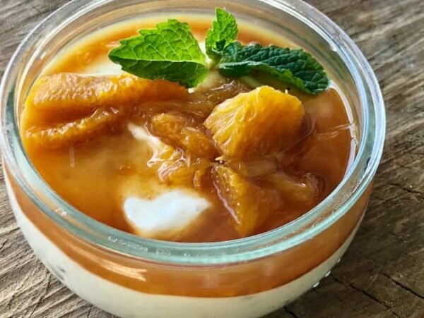 Skinny Greek yogurt pudding with cardamom and oranges topped with fresh mint in small glass dessert bowl on wooden table.