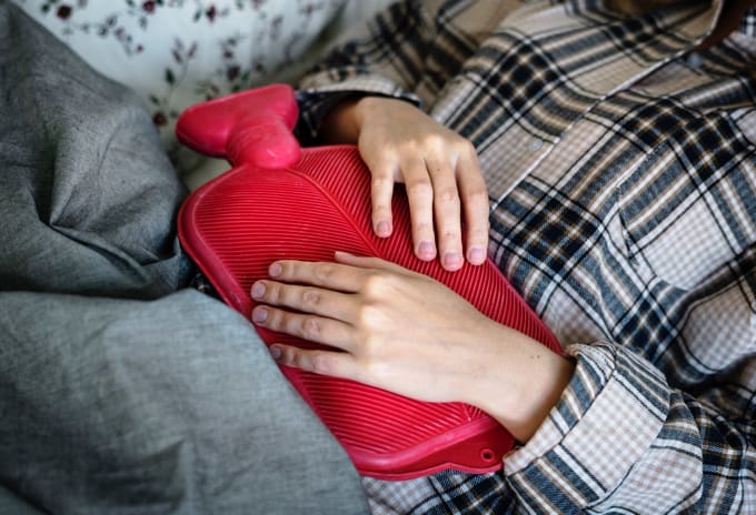 Woman in pajamas lying down with red hot water bottle on her stomach