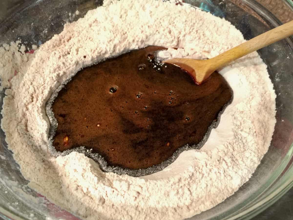 Molasses liquid mixture poured into large bowl of flour for cookie dough with wooden spoon for mixing.