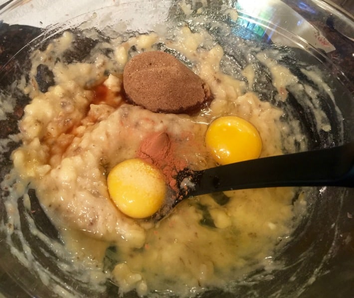 Glass mixing bowl with mashed bananas, two eggs, vanilla, cinnamon and brown sugar.