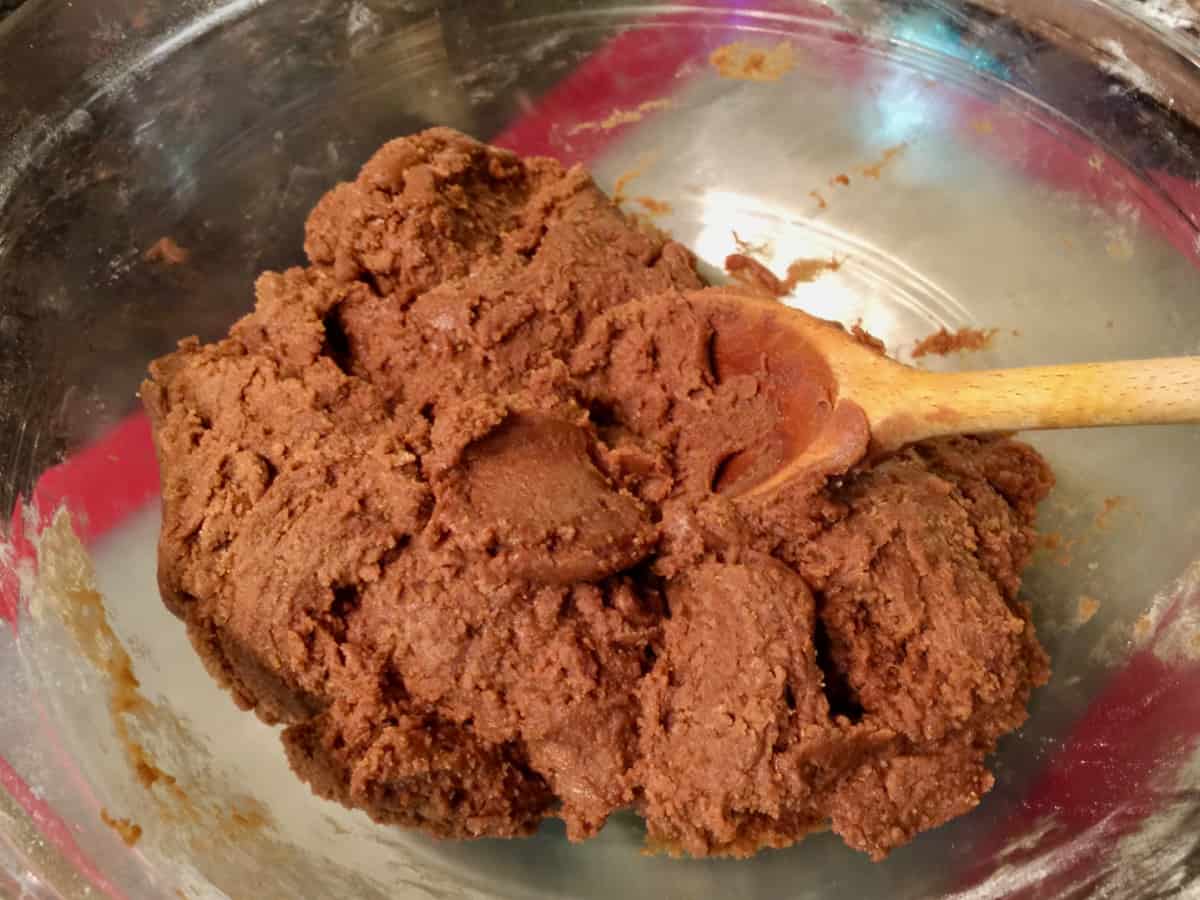 Molasses cookie dough in a large glass mixing bowl with wooden spoon.