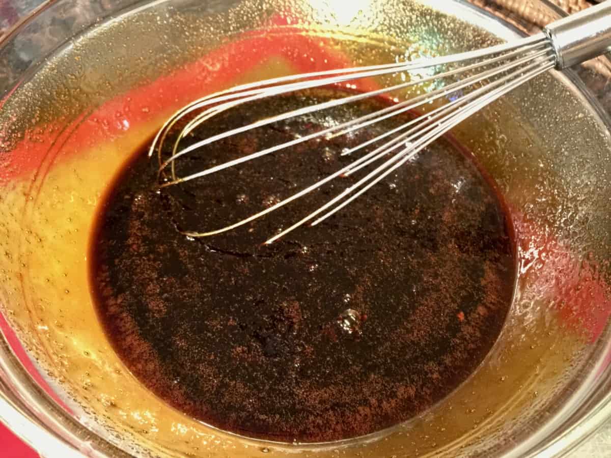 Molasses, eggs, sugar, oil and extracts mixed together in a glass bowl with whisk