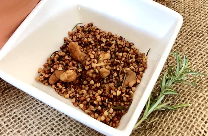 Rosemary Buckwheat Crunch in a square white dish with a sprig of fresh rosemary on a piece of burlap