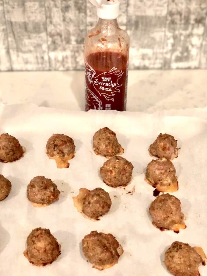 Baked turkey meatballs on parchment paper with Sriracha sauce in the background