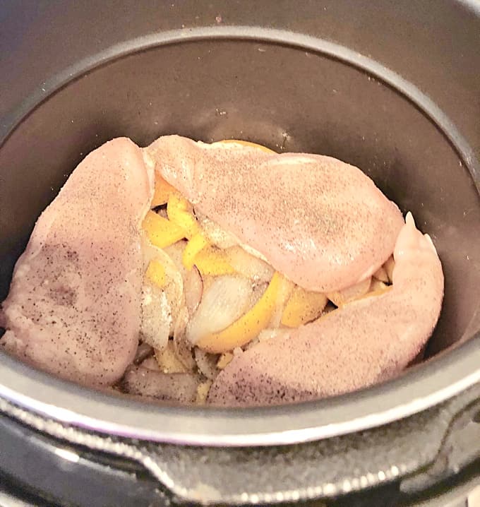 Uncooked chicken breasts with onions in a slow cooker