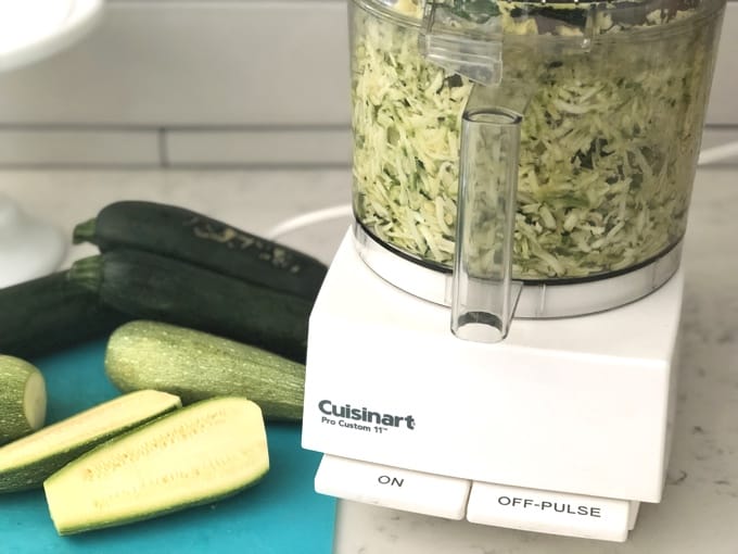 Shredding zucchini in a Cuisinart food processor with zucchini on the counter