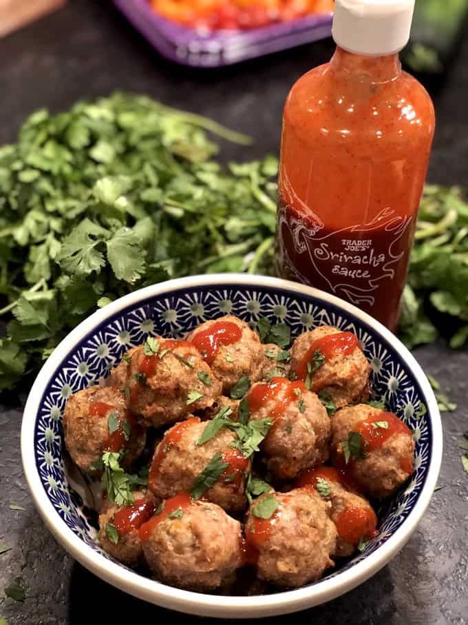 Turkey meatballs in bowl topped with cilantro and Sriracha hot sauce with cilantro and Sriracha bottle in the background