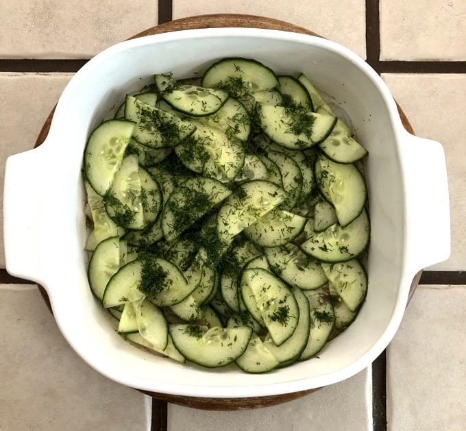Parisian shrimp in casserole dish topped with sliced cucumbers and fresh dill.