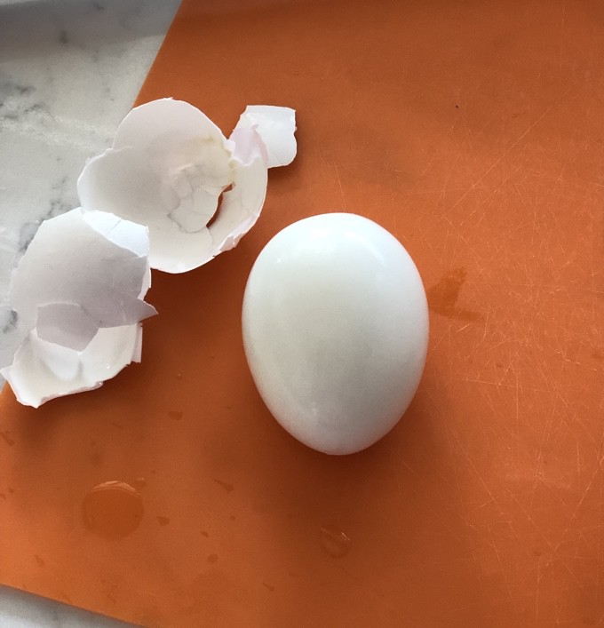 Peeled hard boiled egg on orange cutting mat with egg shell off to the side