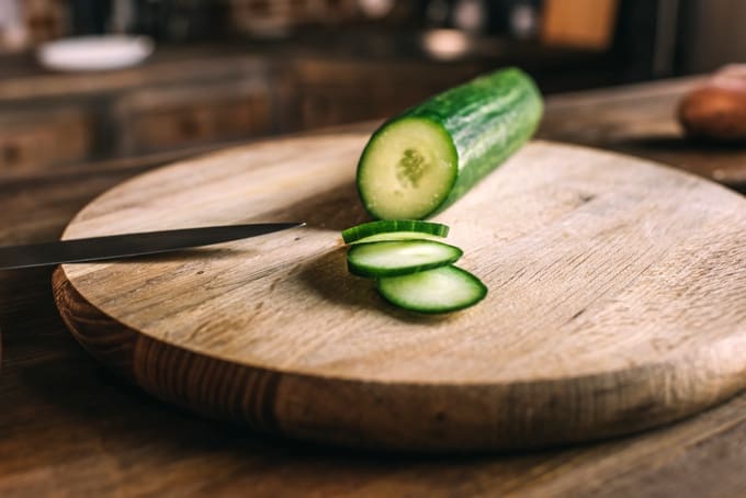 English cucumber with slices on wood cutting board.