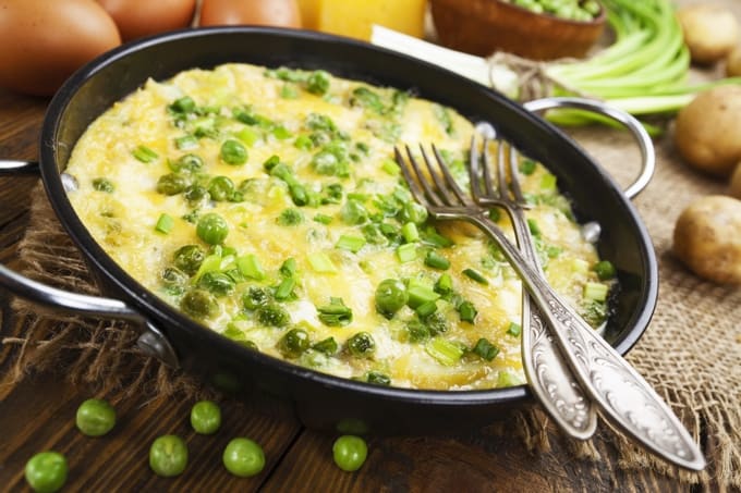 Tortilla pan filled with pea omelet with forks arranged atop. 