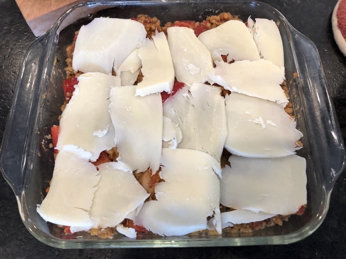 Topping stuffed pepper casserole in baking dish with sliced mozzarella.