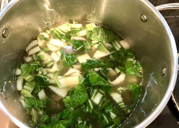 Soup pot with chicken broth, chopped bok choy and spices