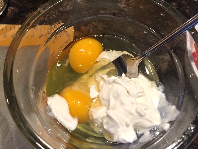 Mixing eggs, milk and yogurt with fork in glass bowl