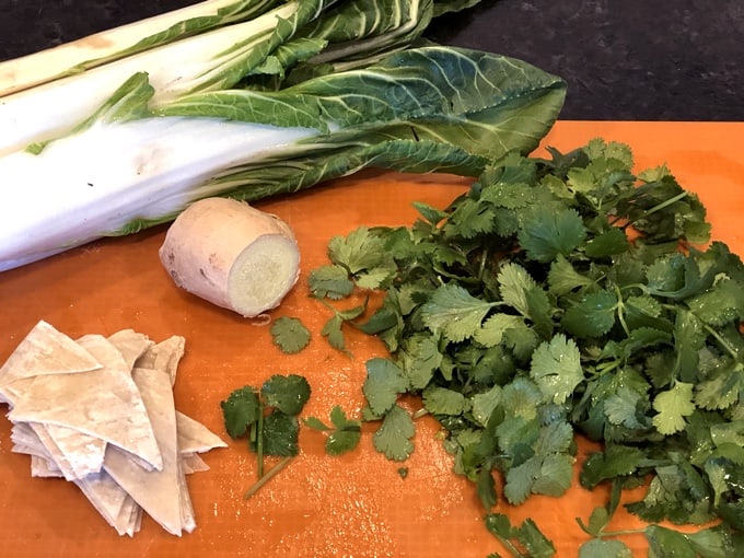 Head of bok choy, fresh ginger, cilantro and wonton wrappers on orange cutting mat
