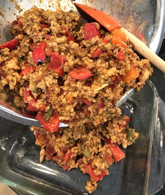 Adding stuffed pepper ingredients from mixing bowl into baking dish with spatula.