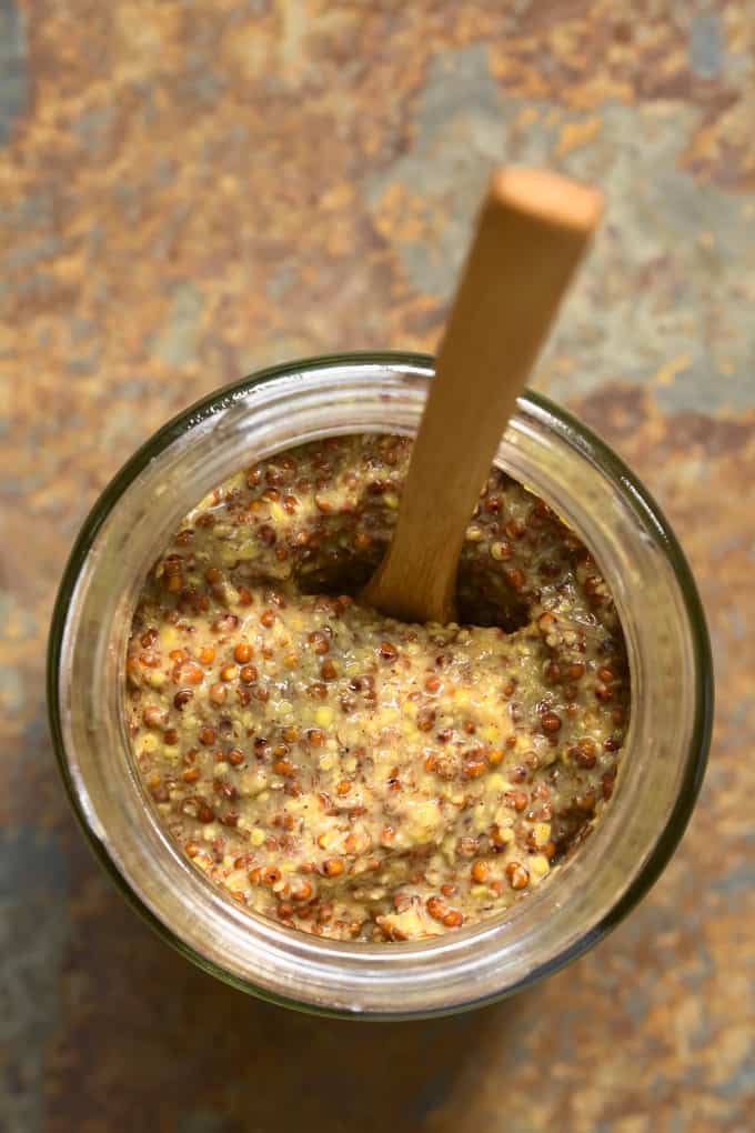 Whole grain mustard in glass jar with wood spoon (from above) on slate counter