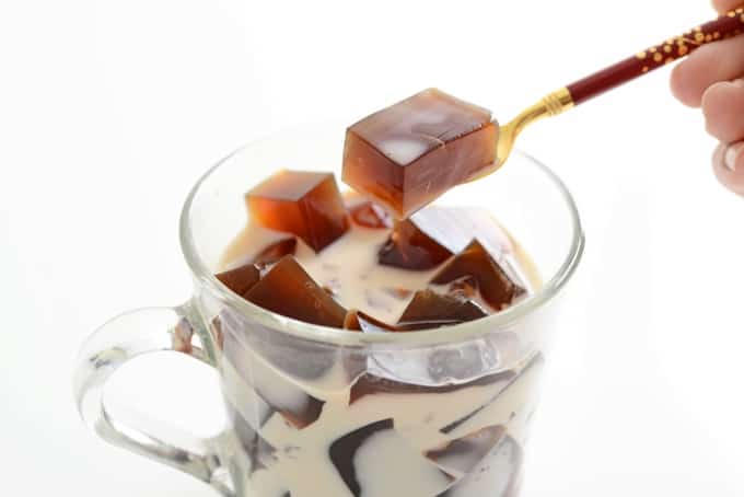 Cubes of coffee jell-o (jelly) in glass mug with milk and spoon.