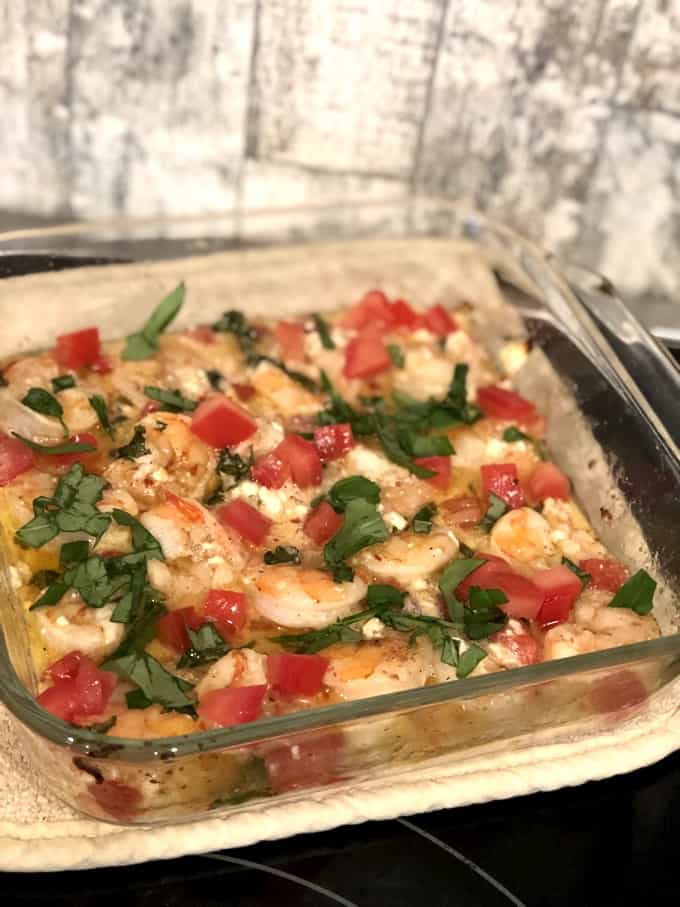 Homemade garlic shrimp in baking dish topped with chopped tomatoes, crumbled Feta cheese and chopped basil.