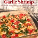 glass baking dish with garlic shrimp garnished with chopped tomato, parsley and feta cheese